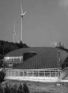 a circular building with solar panels as the roof. Above the building are several windmills.