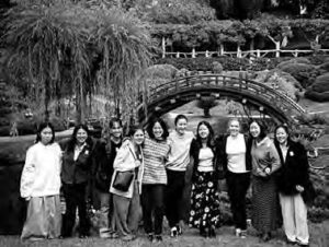 a group of several women stand for a photo in front of a bridge and florals