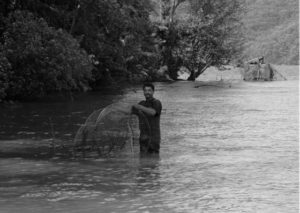 photo of a man standing in a river fishing with a net