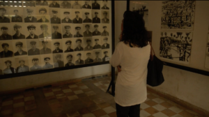 Photo of a woman looking at a wall of photographs of people's faces.