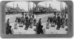 a photo of a wide street with a trolley on it, with several people waiting for it to pass