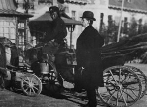 an old timey photo of an old man in a suit getting on a horse drawn carriage driven