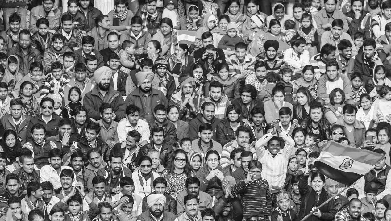 An aerial photograph of a dense crowd of Indian people. One holds an Indian flag. 