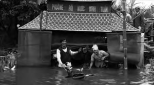 photo of a water puppet theater. two men smile brightly in front of it.