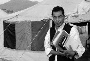 a man holds a stack of books outside a tent