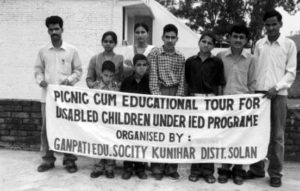 photo of a group of people standing with a banner that reads: picnic cum educational tour for disabled children under IED programme