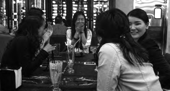 A group of girls sit down at a restaurant table. They are laughing and smiling. 