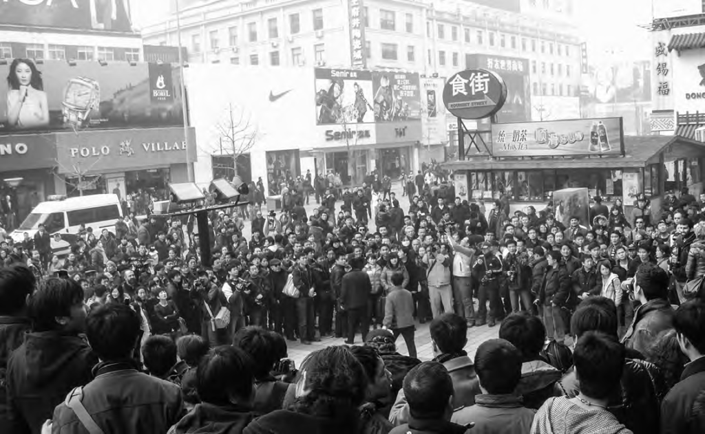 Historical photograph of the Chinese Jasmine Movement. A crowd of people stand in a circle in a metropolitan area. 