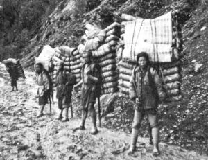 photo of young men holding stacks of bricks on their backs