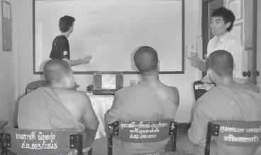 several monk students watch the front board as a teacher writes something