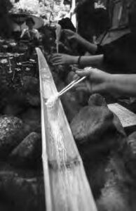 people hold noodles using chopsticks over a thin bamboo slide that has running water through it