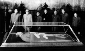 photo of several men looking on at a man's corpse in a glass case