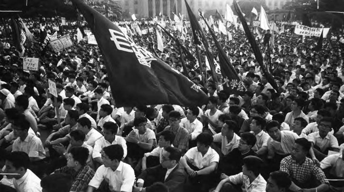 photo of a large group of people sitting in protest, with flags and banners