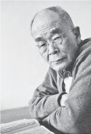 A photograph of D.T. Suzuki as an old man, wearing glasses and with a nearly bald head. He poses with crossed arms, conveying a sense of introspection and wisdom. His pensive facial expression reflects his profound intellectual contributions and deep understanding of Zen Buddhism, cementing his legacy as a prominent figure in the field of philosophy.
