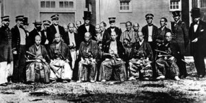 A group of men from the Japanese Embassy standing in two lines. In the front row, Japanese men wearing kimonos sit. In the back row, men in military suits stand. 