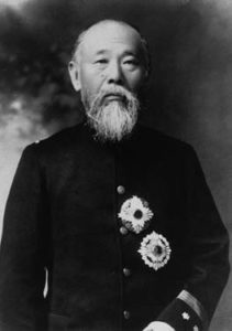 "Portrait of Ito Hirobumi, an elderly man with a bald head and a white beard, looking sternly at the camera. He is dressed in a black military suit adorned with two large military badges."