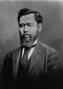 Photograph of Mori Arinori from the waist up. He is a young man wearing a Western style business suit. He has a thick black beard and full head of hair.