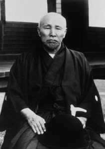 Photograph of Ōkuma Shigenobu sitting. He is a elderly man and is wearing a traditional simple kimono.