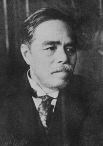 Photograph of Uchimura Kanzo's face. He is a middle aged man with a short, graying mustace. He is wearing a Western style business suit.