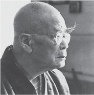 A side profile photograph of D.T. Suzuki, an elderly figure with a shaved head and wearing glasses. He is dressed in a traditional kimono, reflecting his connection to Japanese culture. The image captures his intellectual presence and contemplative demeanor, symbolizing his influential role as a renowned philosopher and interpreter of Zen Buddhism.