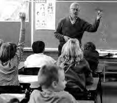 a teacher stands at the front of the room. a student raises their hand. 
