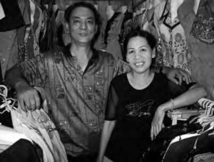 a man and woman smile and pose for a photo among racks of clothing