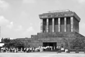 a building with pillars sits above a line of people trying to enter.