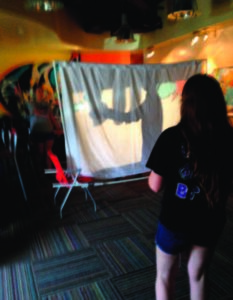 A student watches a puppet play rehearsal. 