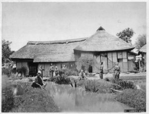 Photo of a Meiji farmer's house with farmers working in the background. 