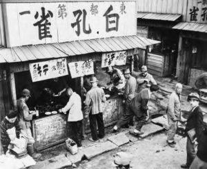 Image of a food stall on the street with some people standing in front of it