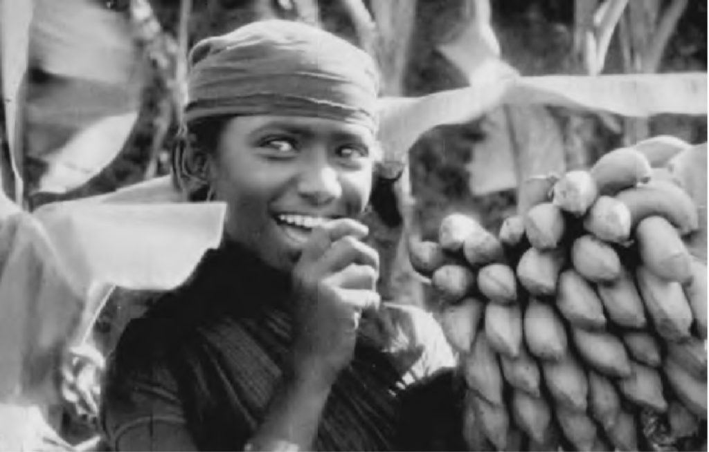 photo of a girl eating a banana from a bushel of bananas