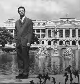 photo of a man in a suit standing in front of a fountain and large palace.