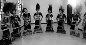 A group of Wa women stand in a circle wearing traditional clothing and participating in a hair swinging dance. 