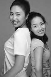 Two Asian young women stand back to back and are smiling. 