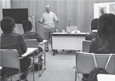 A middle-aged Hirano stands in front of elementary school students as he discusses his experience of surviving the Hiroshima bombing and its aftermath. 