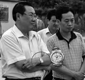 Two middle-aged men holding a diorama of a watch. 