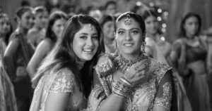 photo of two women smiling, they are wearing saris and in the background are more women in saris 