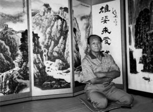 a man sits and crosses his arms in front of large landscape paintings
