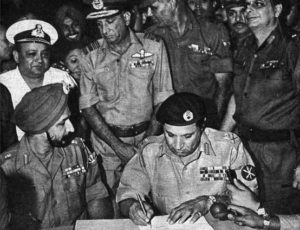 Image shows a military officer signs the instrument while surrounded by soldiers