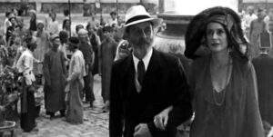 photo of a man and woman in suit and dress walking by people in torn and older clothing (there is a class difference clearly)