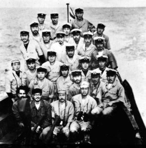 Group of navy men sitting at one end of a boat. 