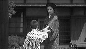 a woman holds a knife up to a child as he takes it in his hand