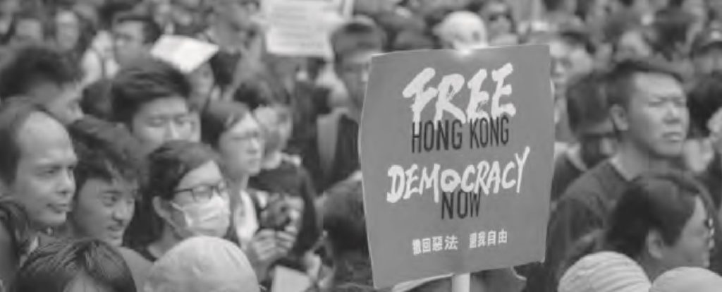 photo of a large group of people with a sign that reads free hong kong, democracy now