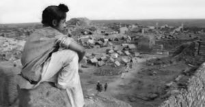 a young boy sits and looks at a camp below