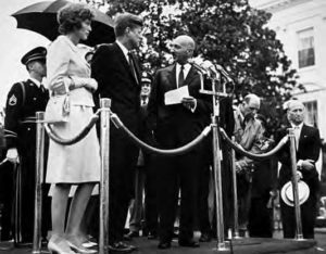 photo of men in suits and a woman in a white dress.