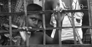 A Rohingya boy looking out from behind a makeshift concentration camp fence