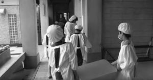 The young students carry their lunch from the kitchen to their classroom.