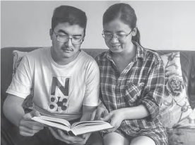 Wang Ping, an Asian woman, and her teenage son sitting together on a couch, engrossed in reading an English book. The scene depicts a cozy and relaxed atmosphere, with a focus on shared learning and the pursuit of knowledge.