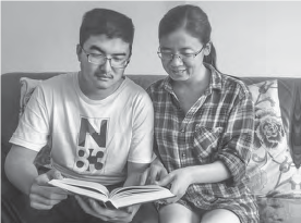 Wang Ping, an Asian woman, and her teenage son sitting together on a couch, engrossed in reading an English book. The scene depicts a cozy and relaxed atmosphere, with a focus on shared learning and the pursuit of knowledge.
