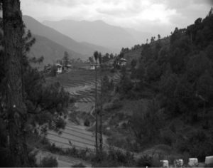 Typical rural setting with small farm dwellings and their steeply terraced hillside fields of rice or barley with higher Himalayan ranges in background.